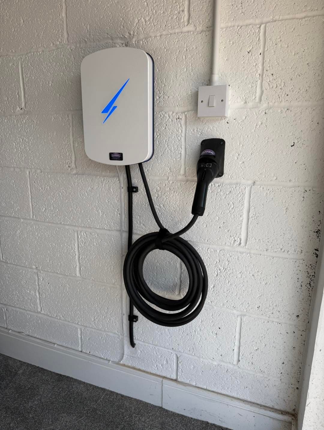 White EV home charger with looped charging cable mounted on a cinder-block wall, installed by Gunning Electrical Services